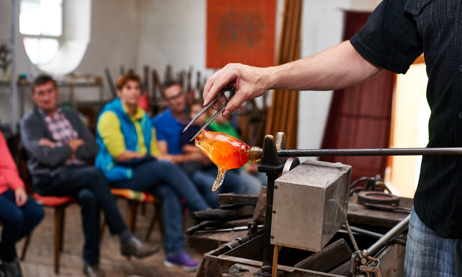 Glasbläser demonstriert vor einer kleinen Besuchergruppe die Herstellung einer Glasfigur in einer Werkstatt im Bayerischen Wald.
